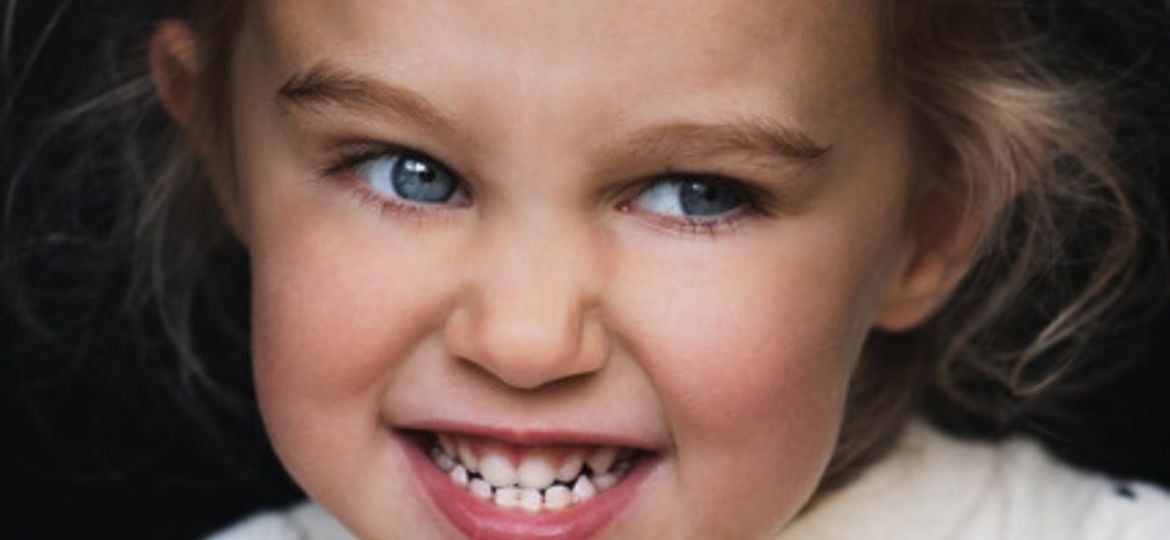 Portret van een lachend meisje met stralende blauwe ogen en mooie glimlach, door De Rooij Fotografie vastgelegd.