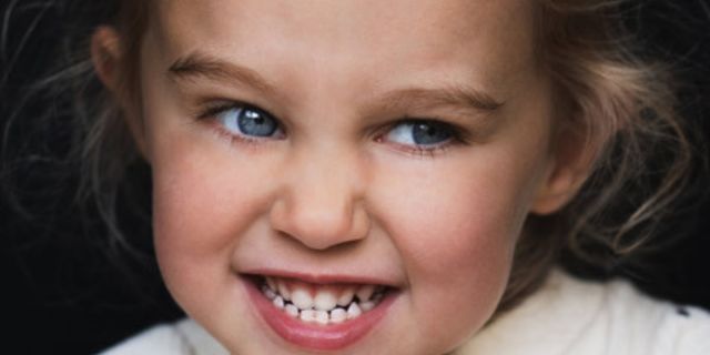 Portret van een lachend meisje met stralende blauwe ogen en mooie glimlach, door De Rooij Fotografie vastgelegd.